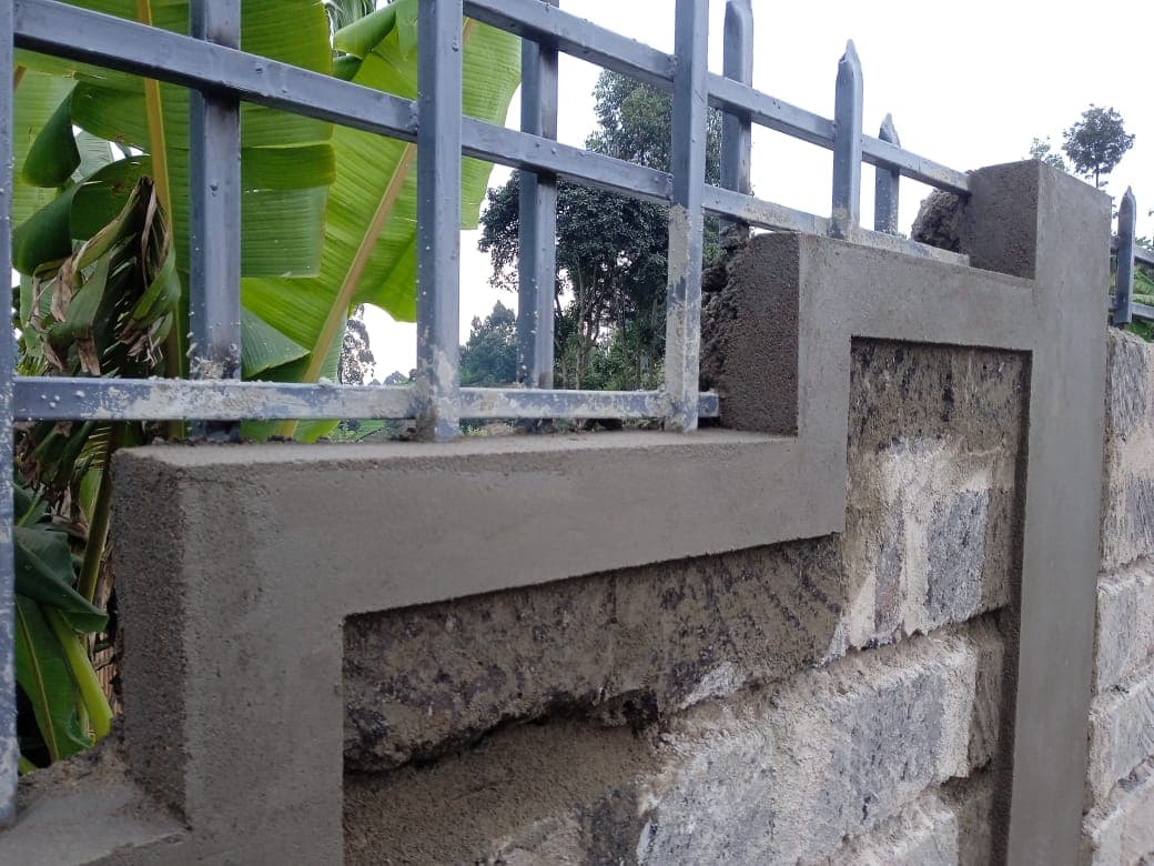 Close-up detail of corner joint showing grooved block texture, plastered cap and metal railings with banana leaves