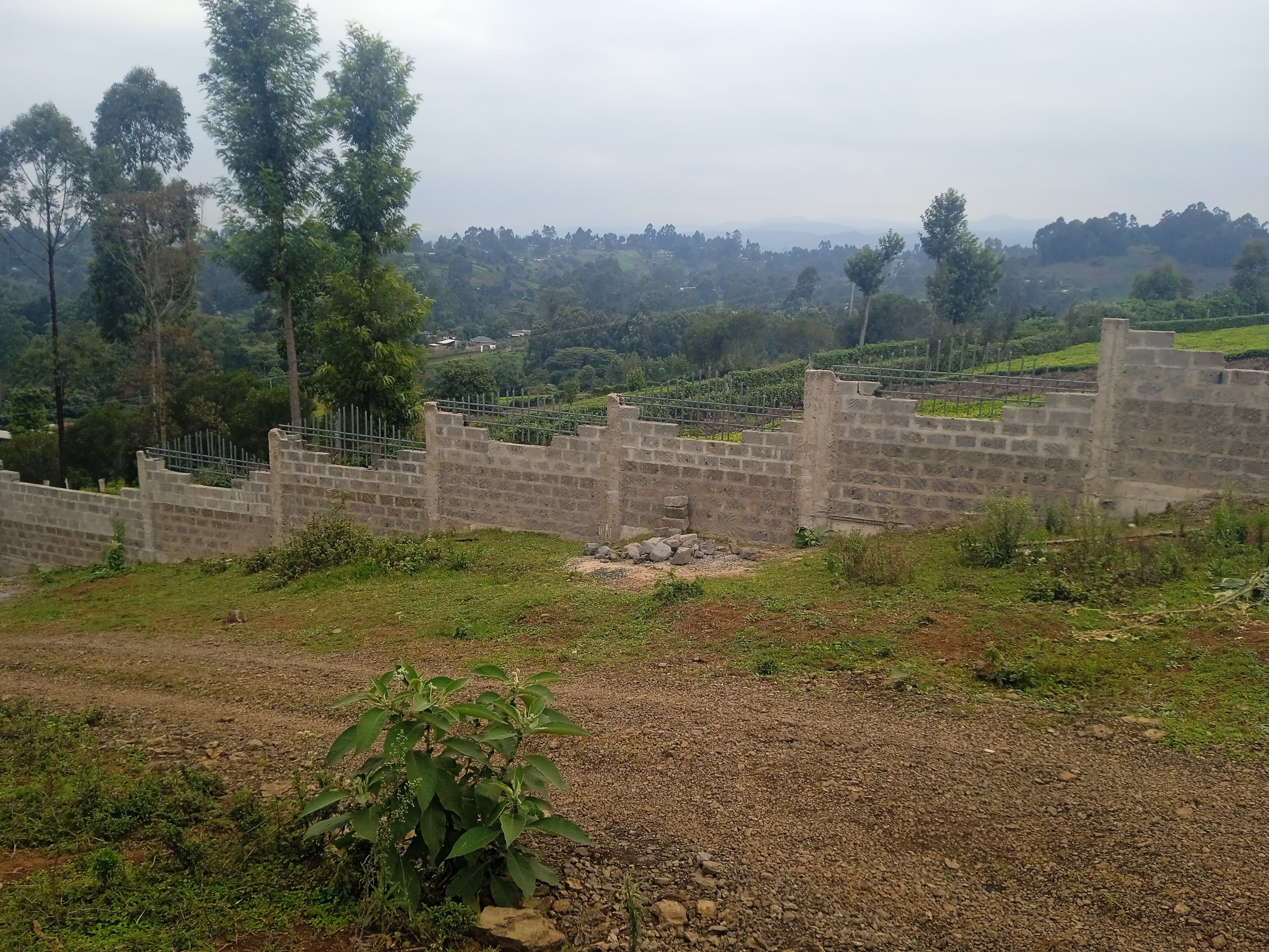 Completed wall sections with metal railings and pillars overlooking misty valley, stone pile in grassy area