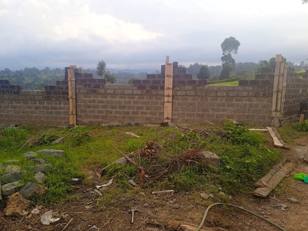 Block wall with wooden pillar supports and formwork still in place, grassy construction site