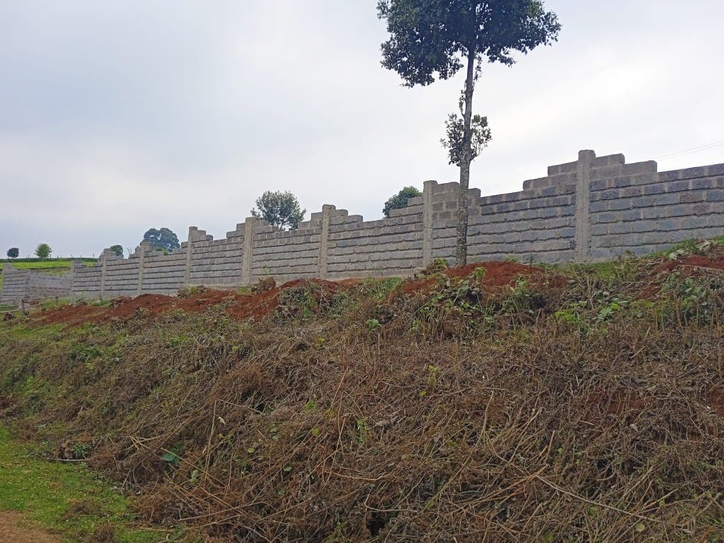 Perimeter wall with pillars on hillside with freshly excavated red soil and surrounding vegetation