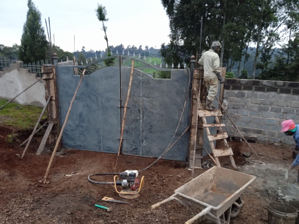 Worker on ladder installing arched decorative gate with compactor equipment