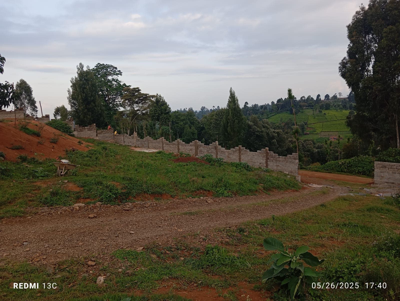 Wide panoramic view of perimeter wall with battlements stretching across property, green hills and wheelbarrow visible
