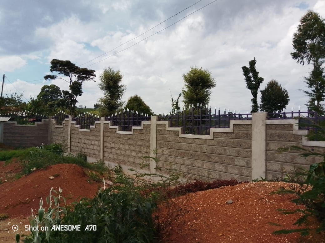 Panoramic view of completed perimeter wall with stepped stonework and metal fencing