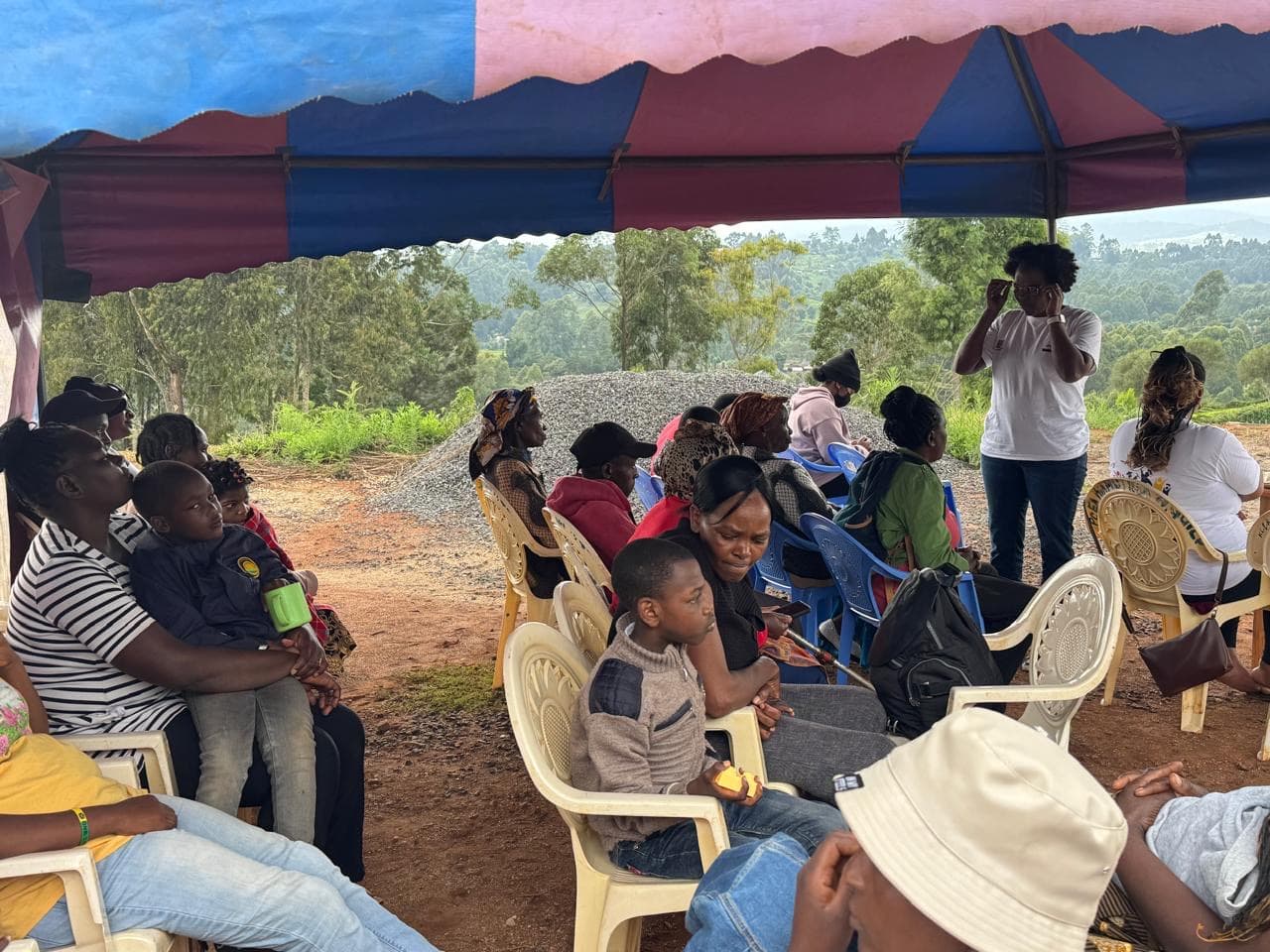 Githima family gathering under tent with community members seated