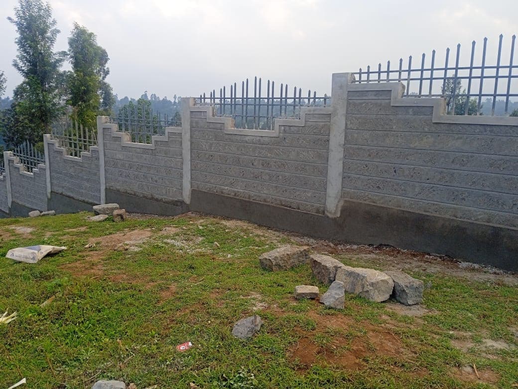 Long curved section of finished wall with decorative stepped tops, metal railings, stones and cement bag on grass