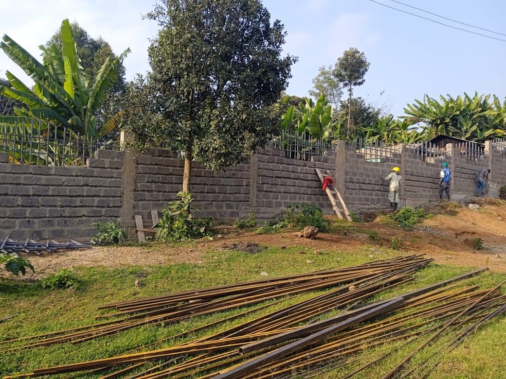 Steel reinforcement bars laid out on grass with worker in yellow hard hat on ladder, metal railings installed on wall