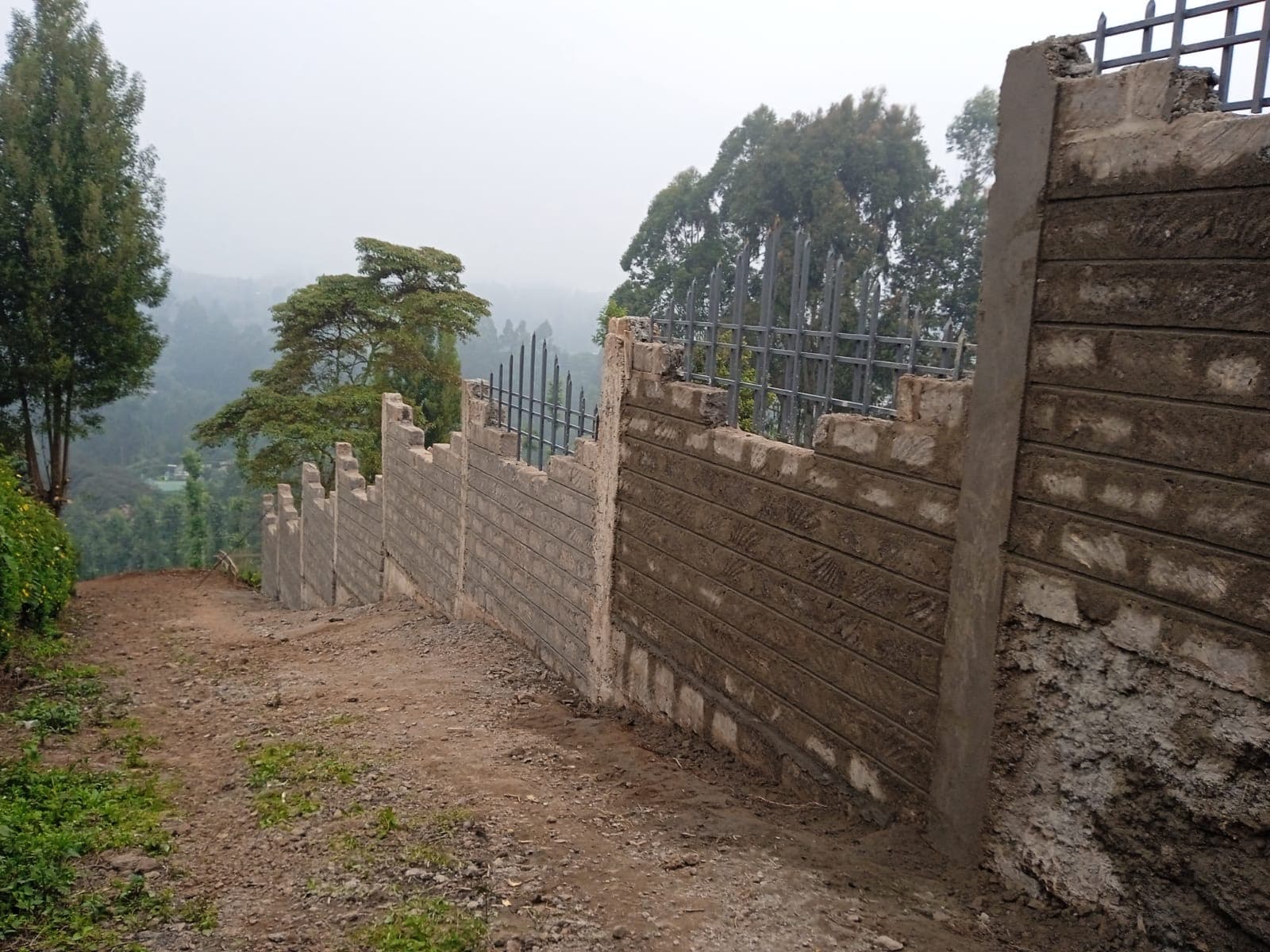 Long stretch of perimeter wall with pillars and metal railings descending along hillside with misty valley
