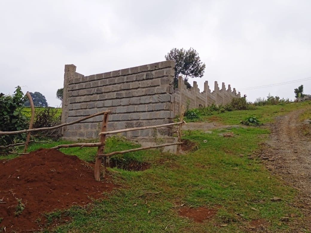 Corner section of perimeter wall with wooden safety barrier and green fields extending into distance