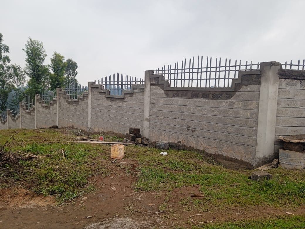 Completed perimeter wall with decorative stepped top and metal security railings, stone blocks with grooves pattern
