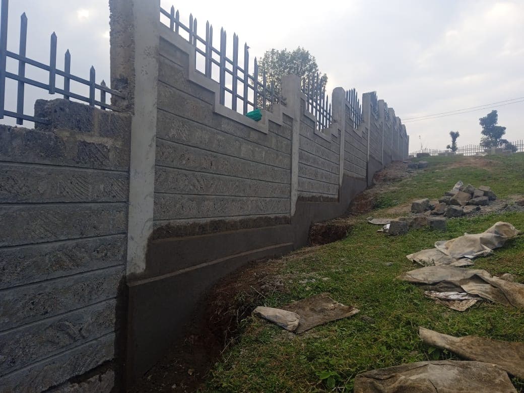 Long curved section of finished wall with decorative stepped tops, metal railings, and foundation drainage channel