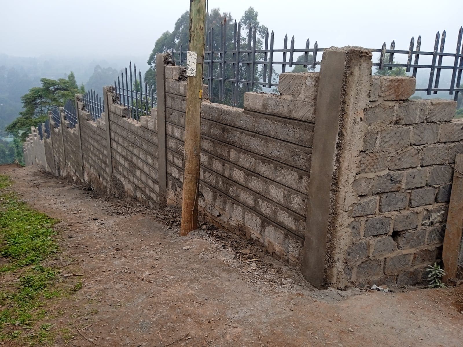 Close-up of block wall with decorative grooves and metal security railings, misty valley view in background