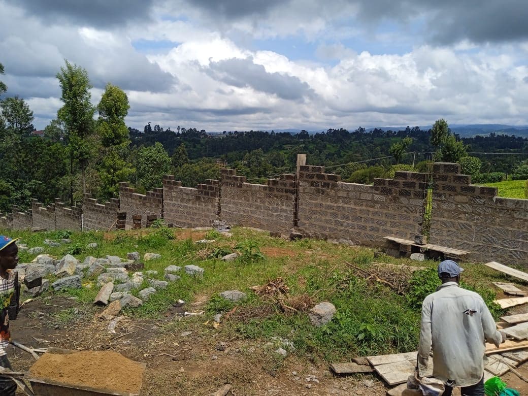Workers on construction site with perimeter wall in background, stones and building materials visible