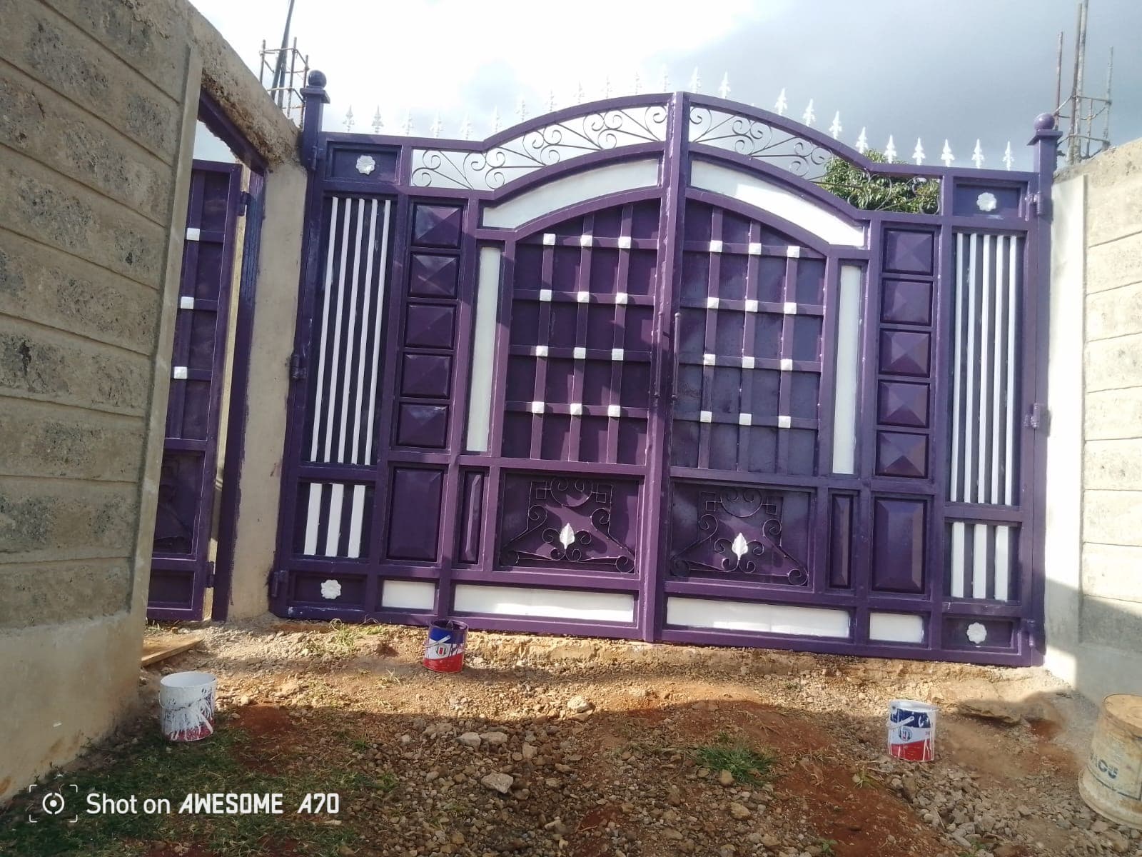 Completed main entrance gate painted in purple and white with arched design and decorative scrollwork