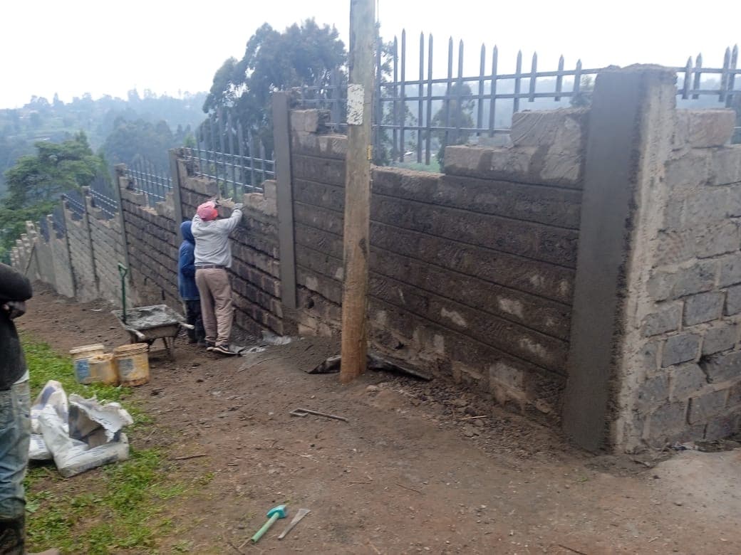 Workers constructing perimeter wall with metal fencing
