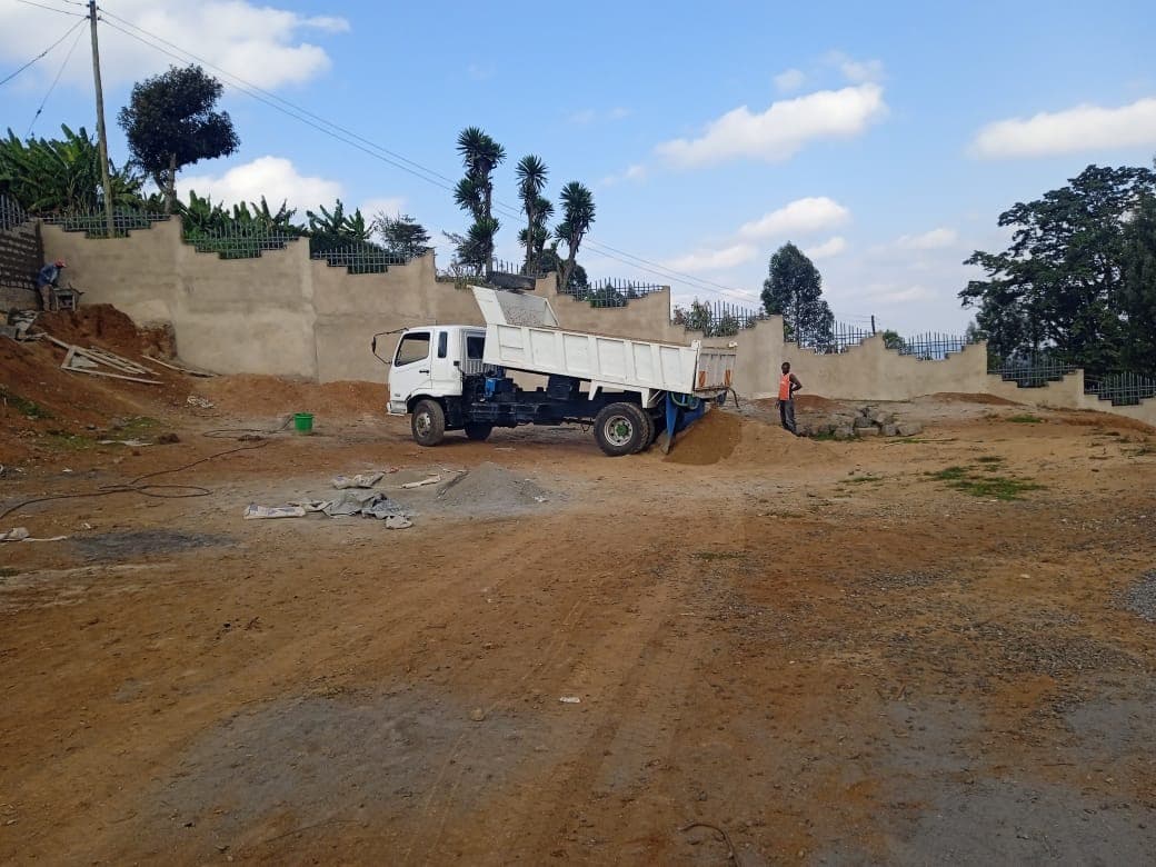 White delivery truck unloading sand at construction site with plastered walls and metal railings in background